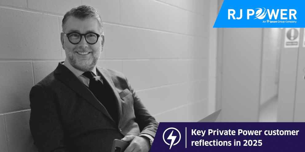 Man with glasses and suit sat and smiling at camera.