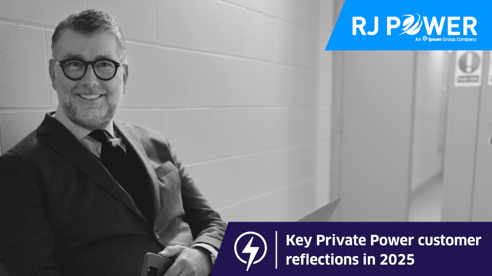 Man with glasses and suit sat and smiling at camera.